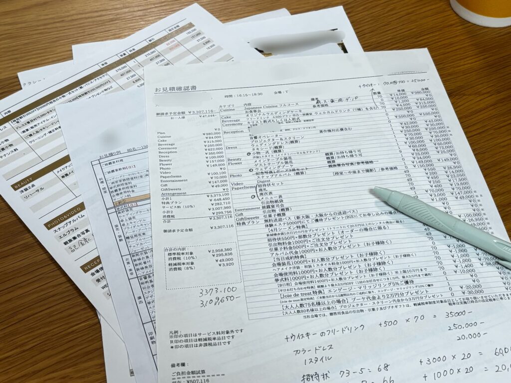 実際のブライダルフェアで受け取った5つの式場の見積書を並べて比較した写真。式場名は伏せ、総額や特典内容を見比べた手書きメモも添えている